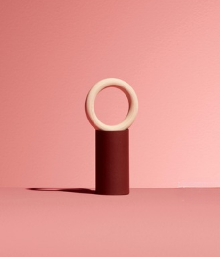 Base cylindrique opaque bordeaux, surmontée d'un anneau beige. Design épuré.